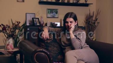 一个穿着棕色西装的欧洲年轻怀孕女孩坐在家里的扶手椅上，用手指<strong>抠</strong>鼻子